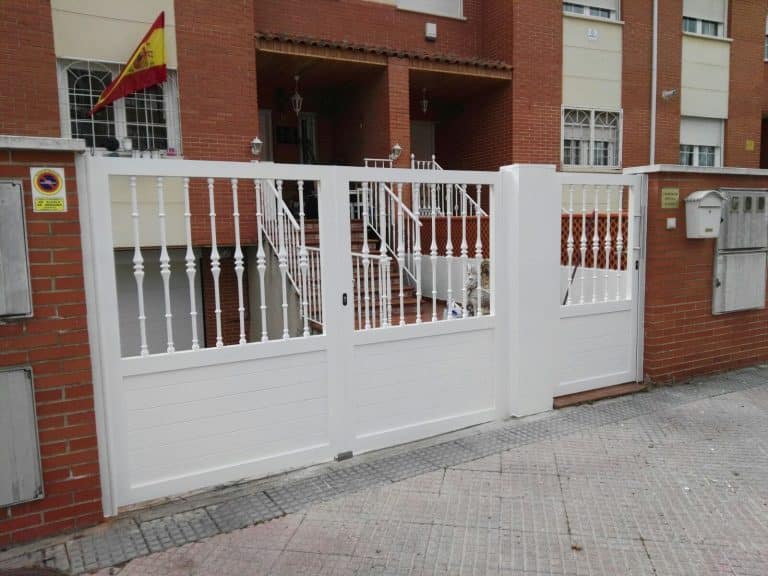 Cancela y valla de hierro blancas con barrotes torneados en una urbanización