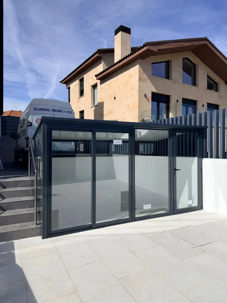 Caseta de aluminio gris antracita con correderas de vidrio que cierra el acceso a una escalera en el patio de un chalet