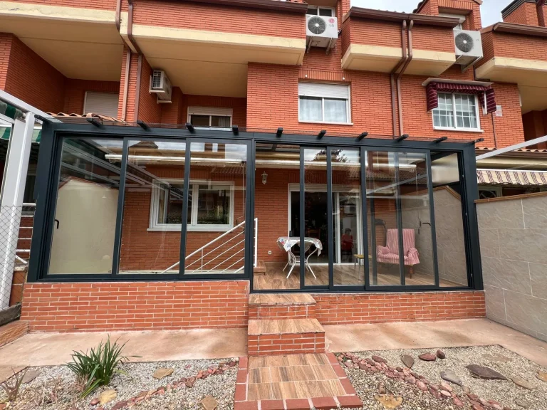 Porche trasero de una casa adosada cerrado con aluminio gris antracita y correderas de vidrio sobre murete de ladrillo