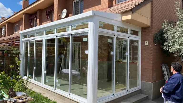 Cerramiento de porche con correderas de aluminio blanco y techo acristalado en una casa de ladrillo