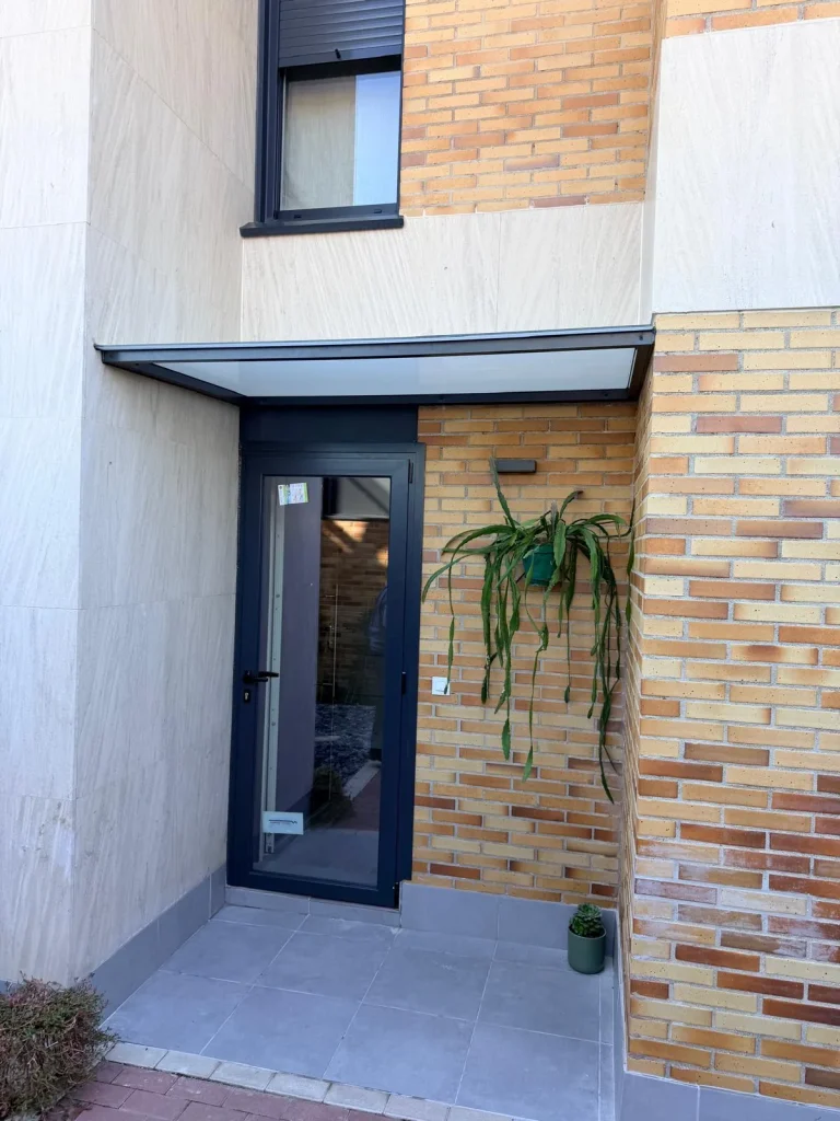 Contrapuerta de aluminio gris antracita con marquesina de vidrio sobre la entrada de una vivienda