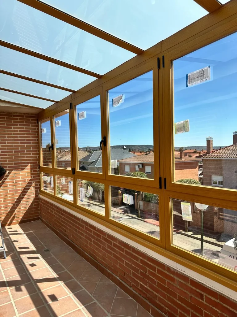 Ventanas correderas de aluminio imitación madera que cierran una terraza sobre murete de ladrillo visto