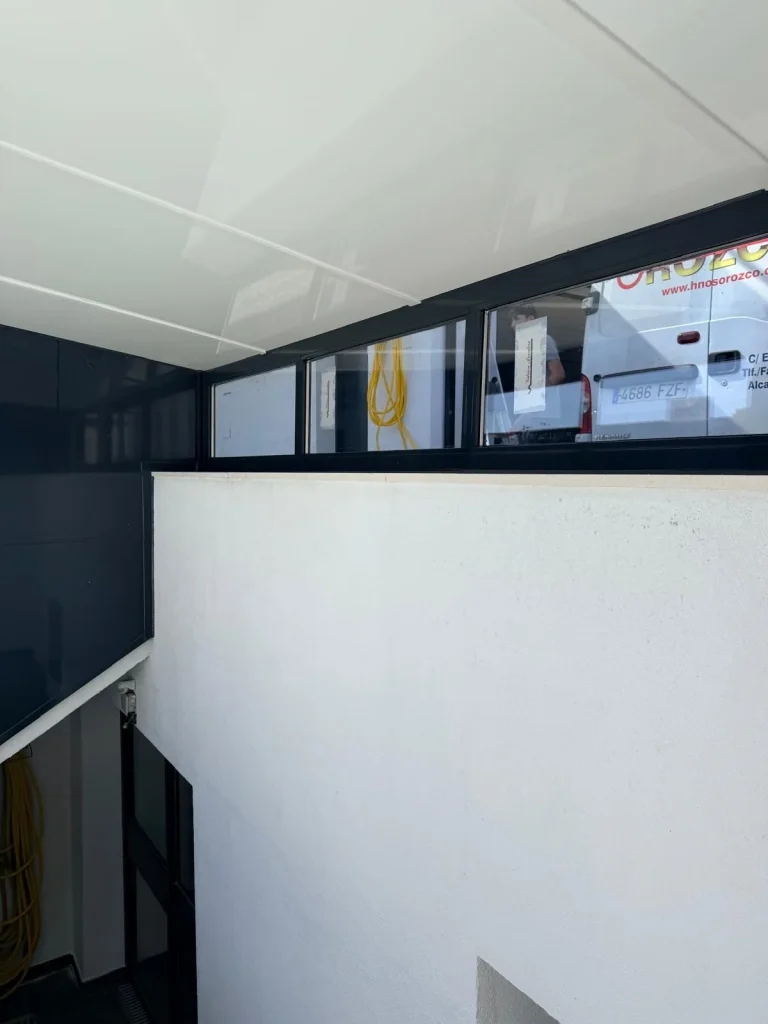 Interior de un cerramiento de escalera con fijos acristalados de aluminio antracita sobre el muro y techo de panel