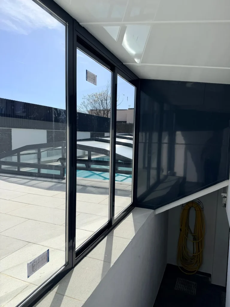 Vista interior de un cerramiento de aluminio antracita con hojas correderas de vidrio y techo de panel blanco