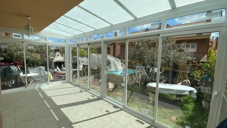 Porche acristalado con perfiles de aluminio blanco, techo de vidrio y vistas al jardín
