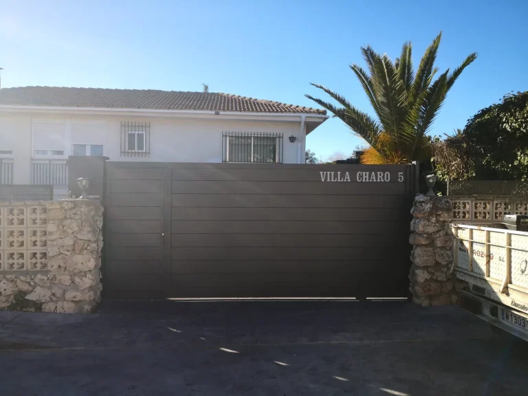 Puerta corredera de vehículos de aluminio gris oscuro de lamas horizontales en la entrada de un chalet