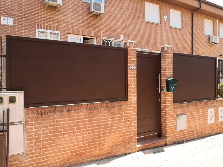 Paneles de vallado de aluminio marrón sobre muro de ladrillo con puerta peatonal a juego