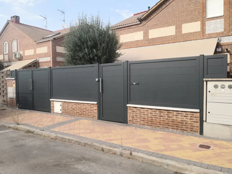 Vallado de parcela con paneles de aluminio gris, puerta peatonal y puerta de vehículos sobre murete de ladrillo